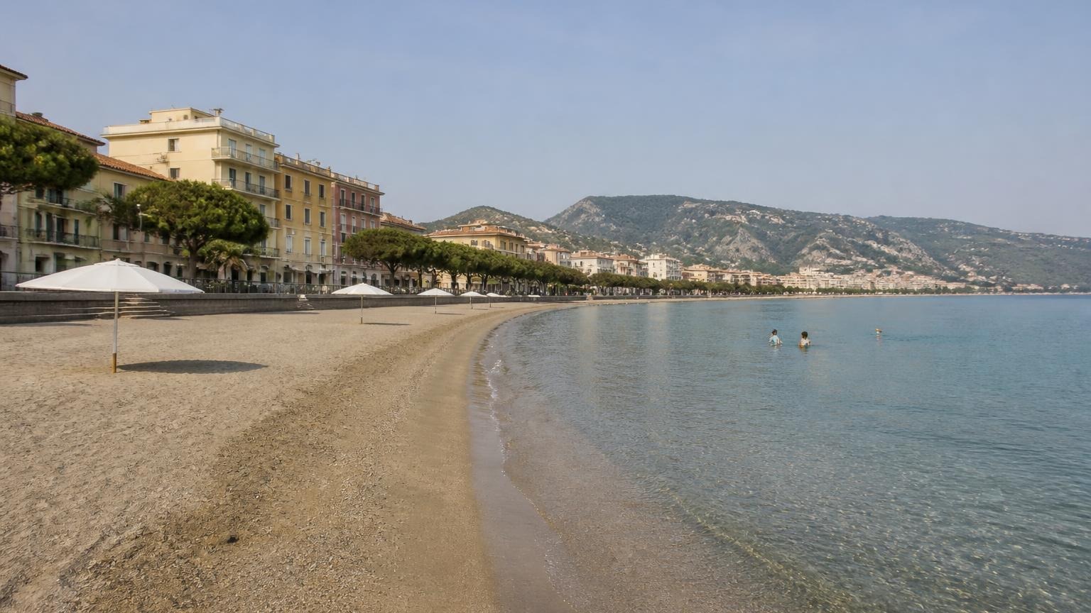 Breiter flacher Sandstrand mit Promenade und Kindern im seichten Wasser