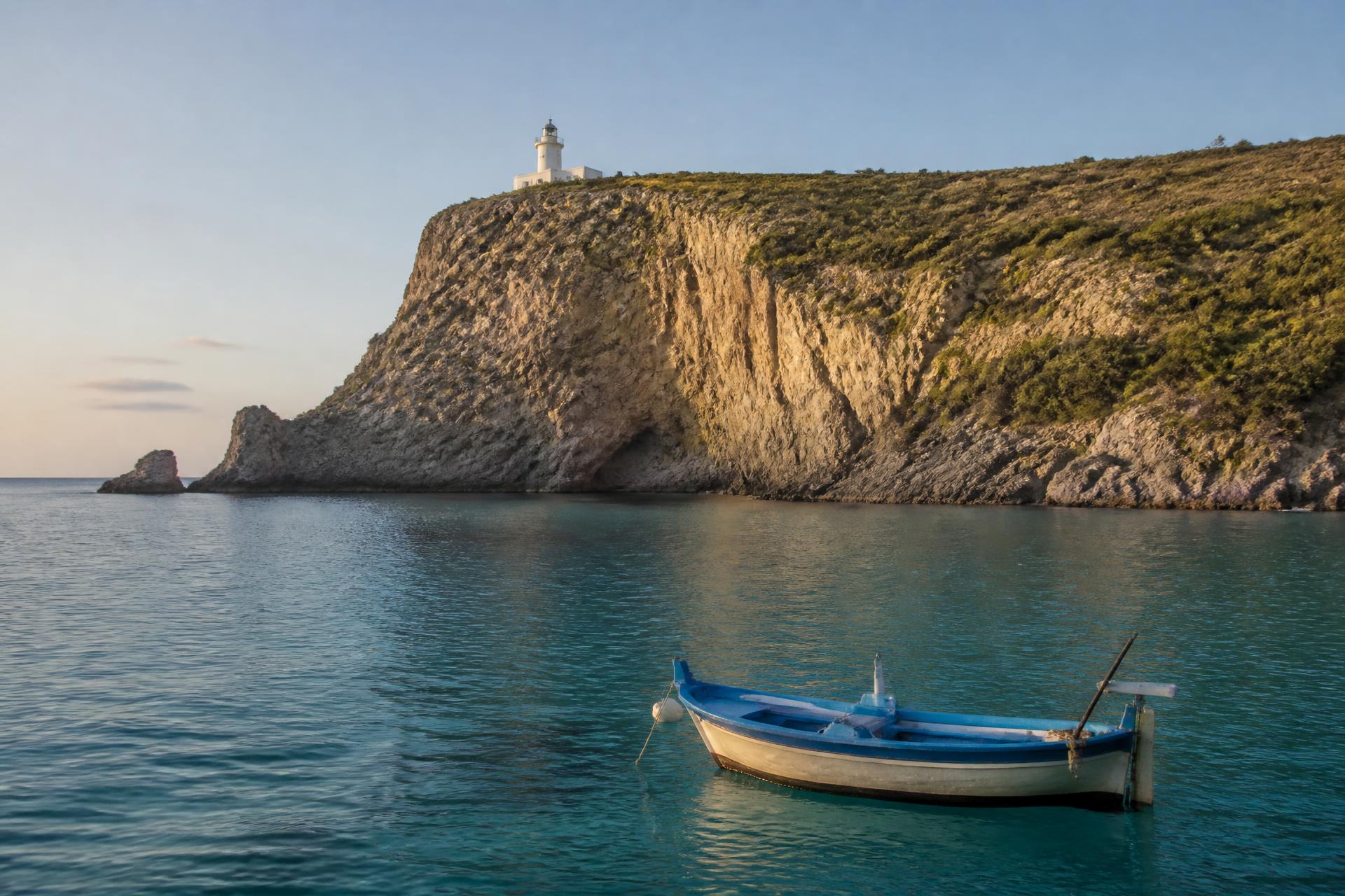 Capo Palinuro mit Leuchtturm auf der Steilküste, davor ein Fischerboot im türkisblauen Meer